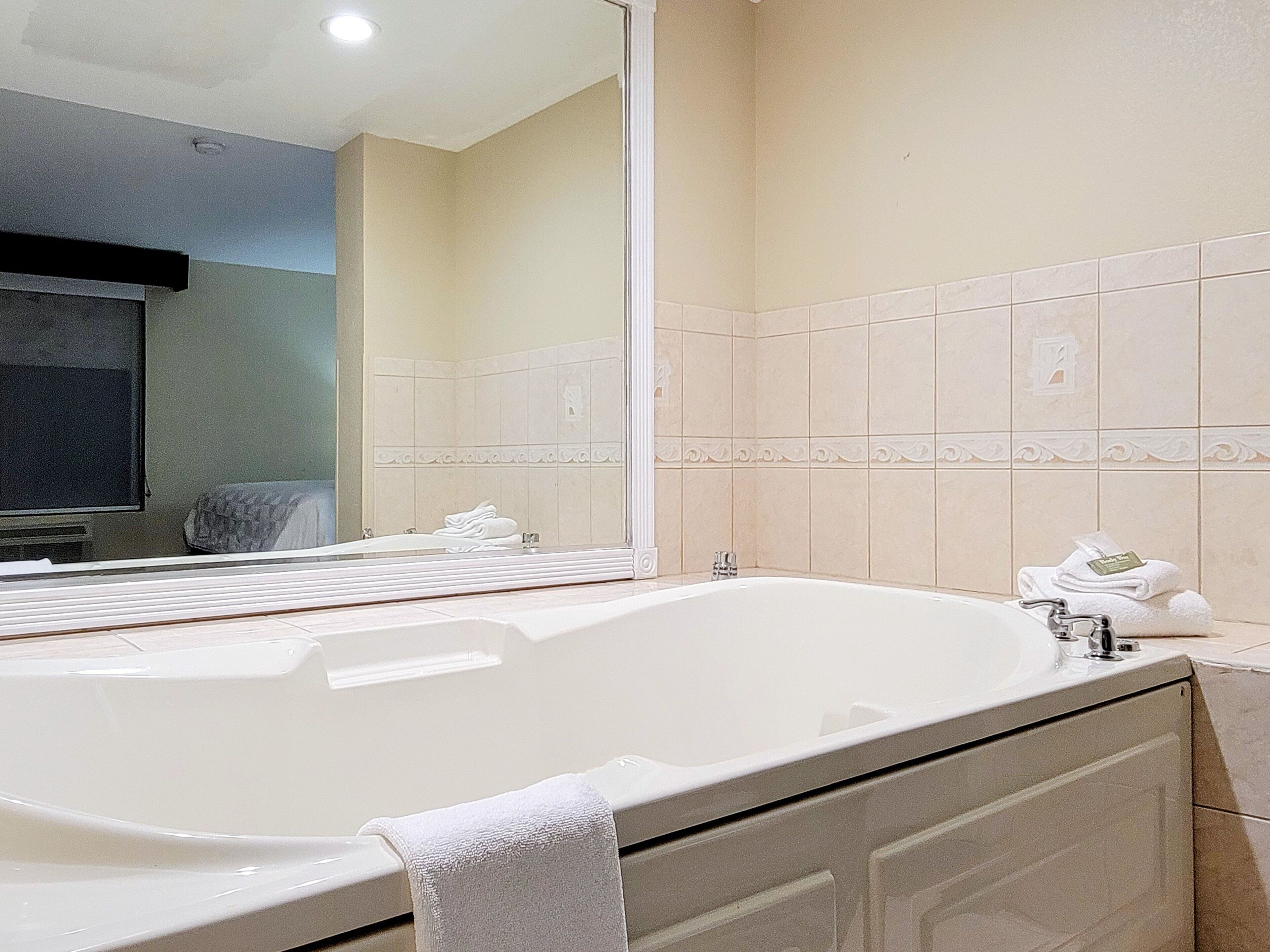 Une salle de bain avec une grande baignoire, un miroir et un mur recouvert de carreaux.