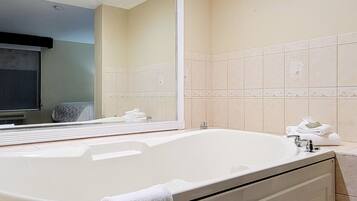 Une salle de bain avec une grande baignoire, un miroir et un mur recouvert de carreaux.