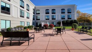 Un patio con mesas al aire libre, un edificio con varias ventanas y un cielo azul despejado.