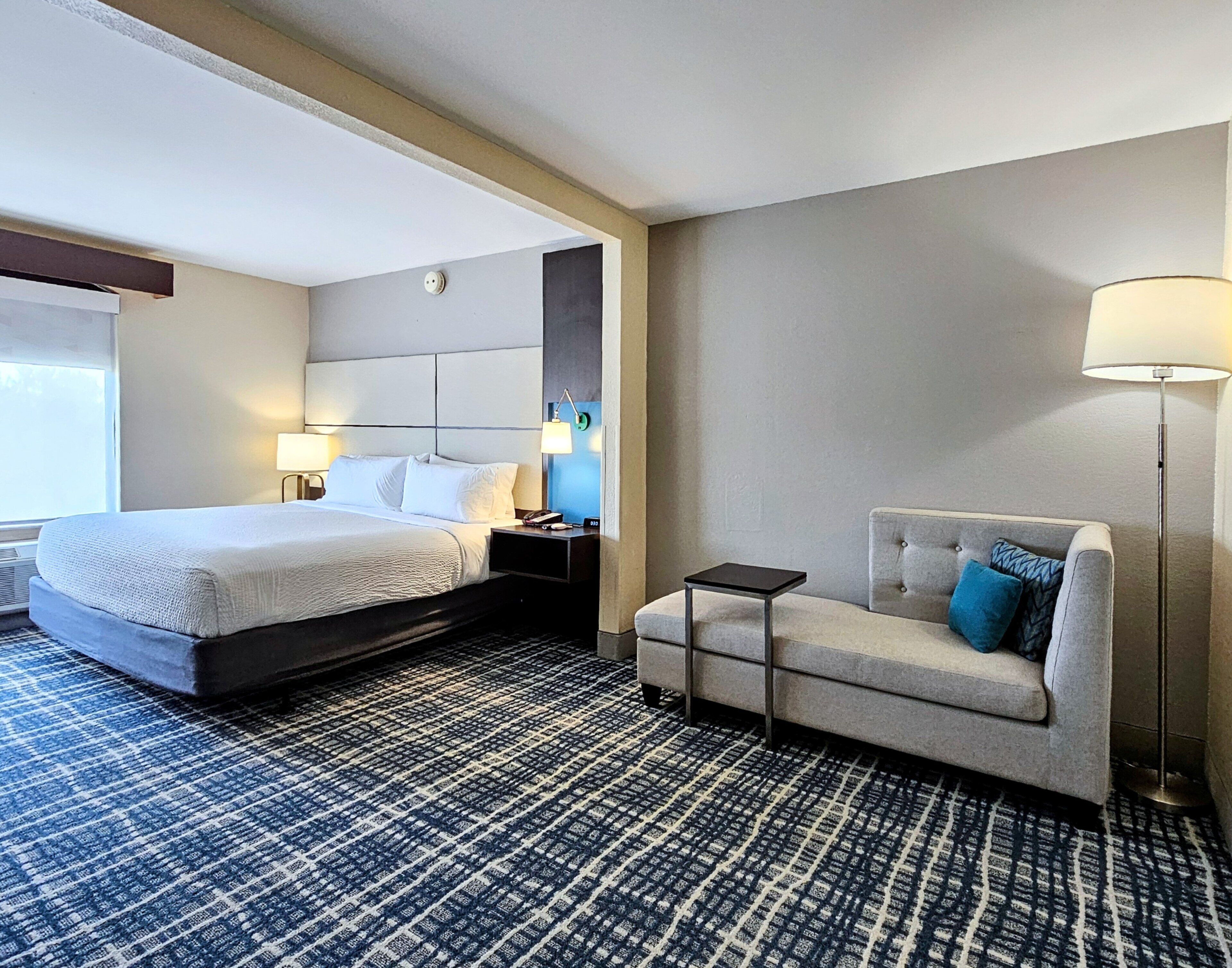 Una habitación de hotel con una cama grande, un sofá, una mesita y una lámpara.
