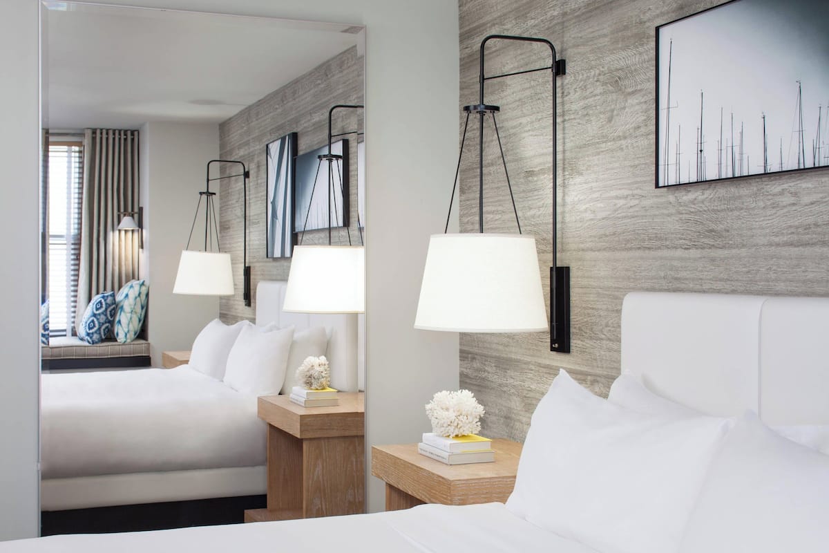 A hotel room with a large bed, two bedside tables with lamps, a mirror, and a wall-mounted artwork.