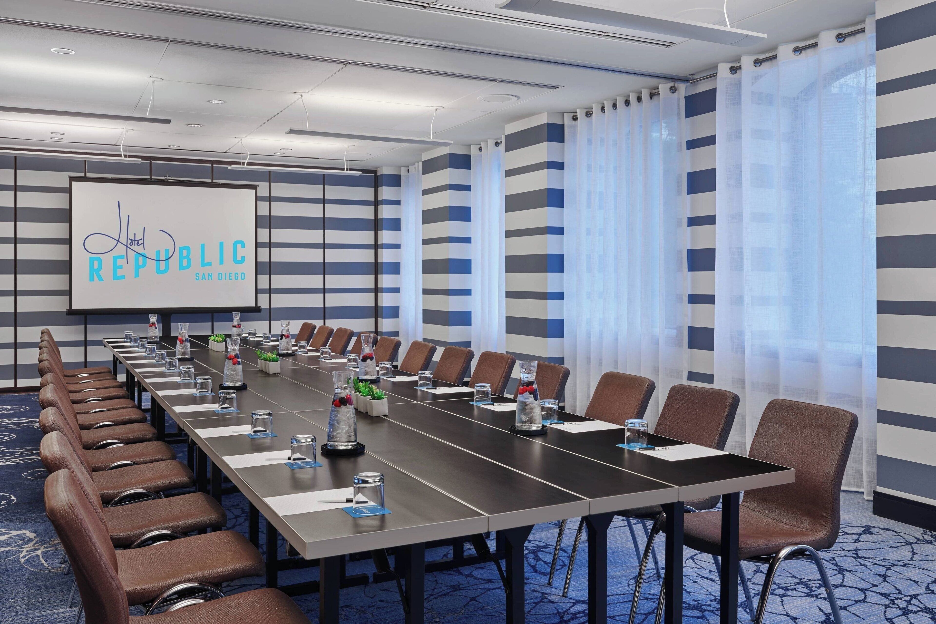 A conference room with a long table, chairs, and a screen displaying "Republic San Diego".