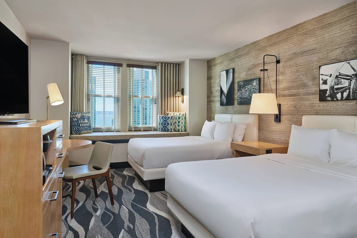 A hotel room with two beds, a desk, a chair, a TV, and a window with curtains.
