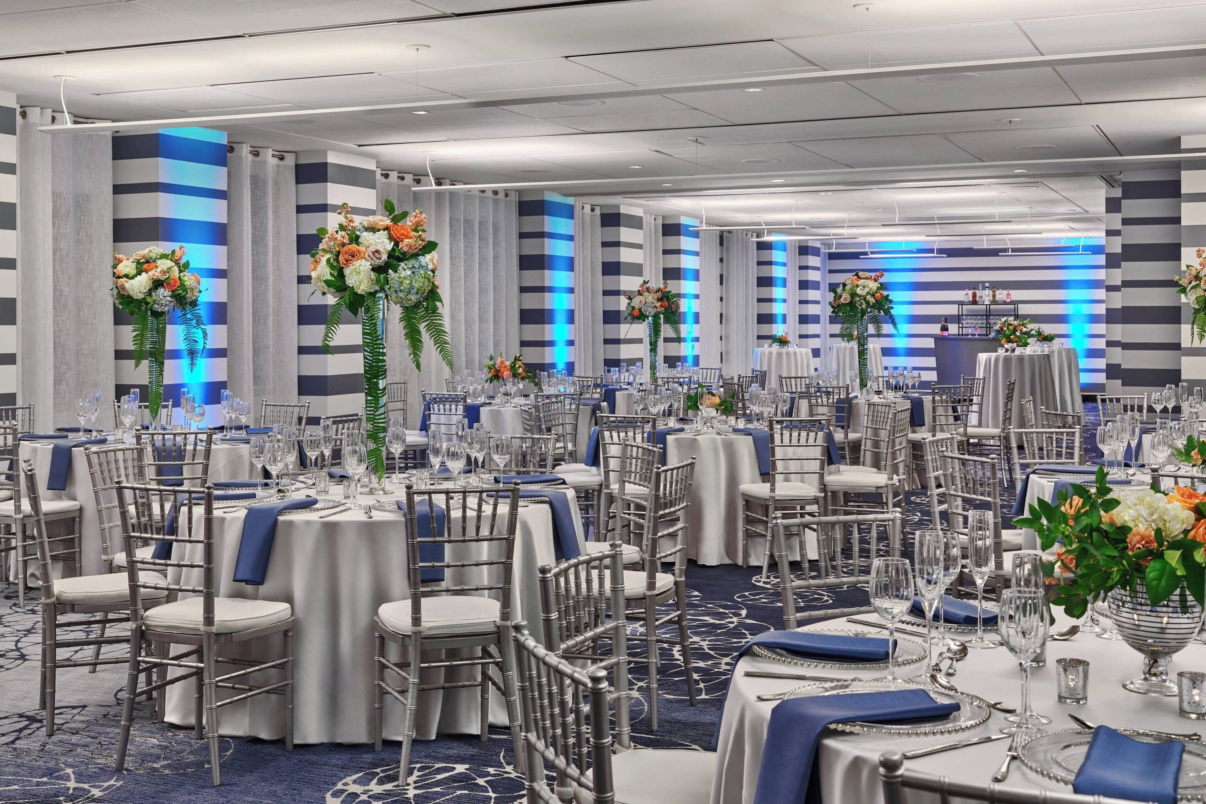 A banquet hall with round tables, chairs, and floral centerpieces.