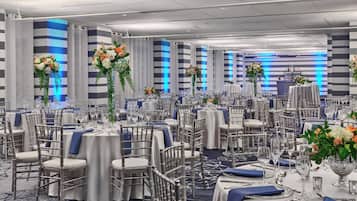 A banquet hall with round tables, chairs, and floral centerpieces.