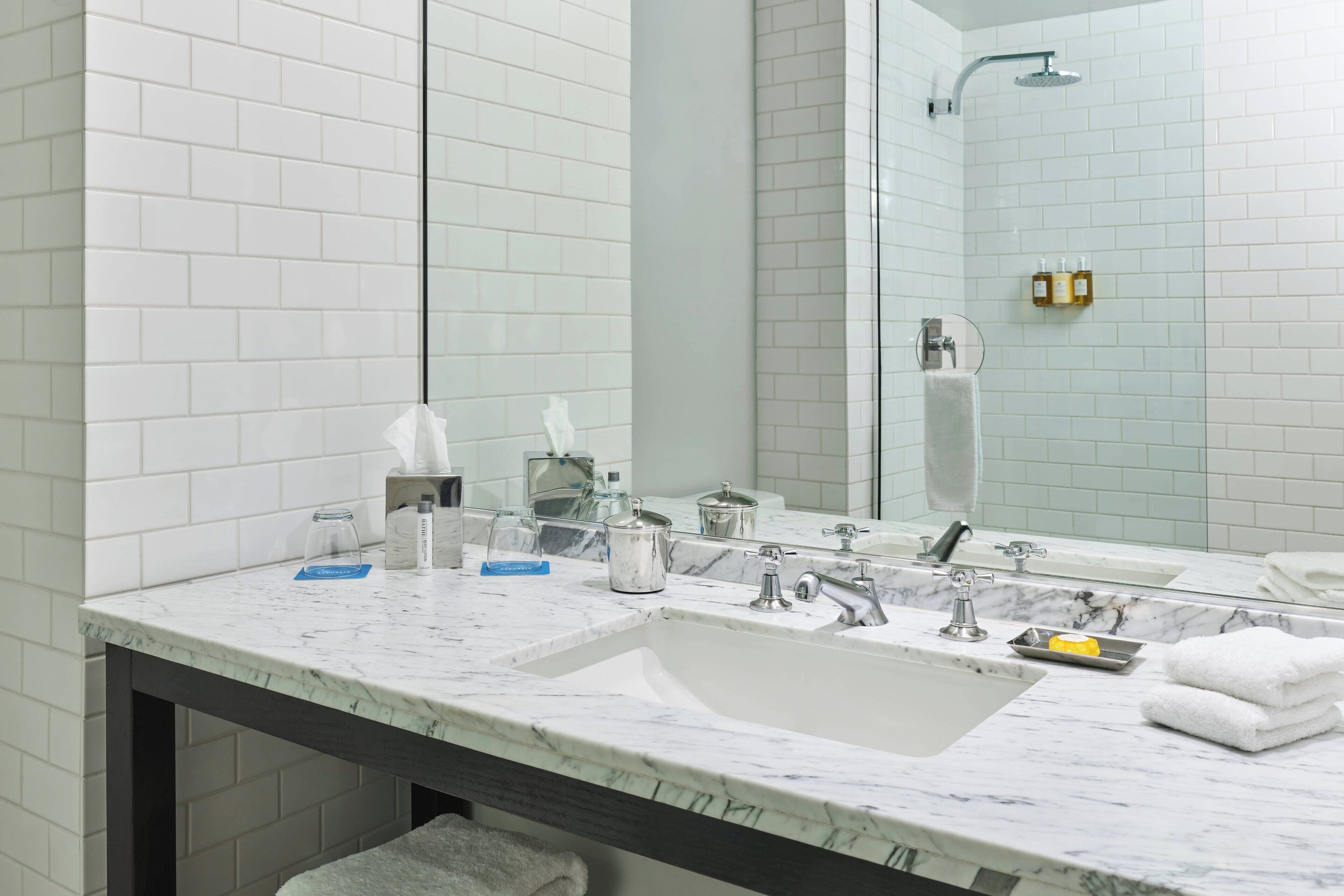 A bathroom with white tiled walls, a marble sink, and a large mirror.