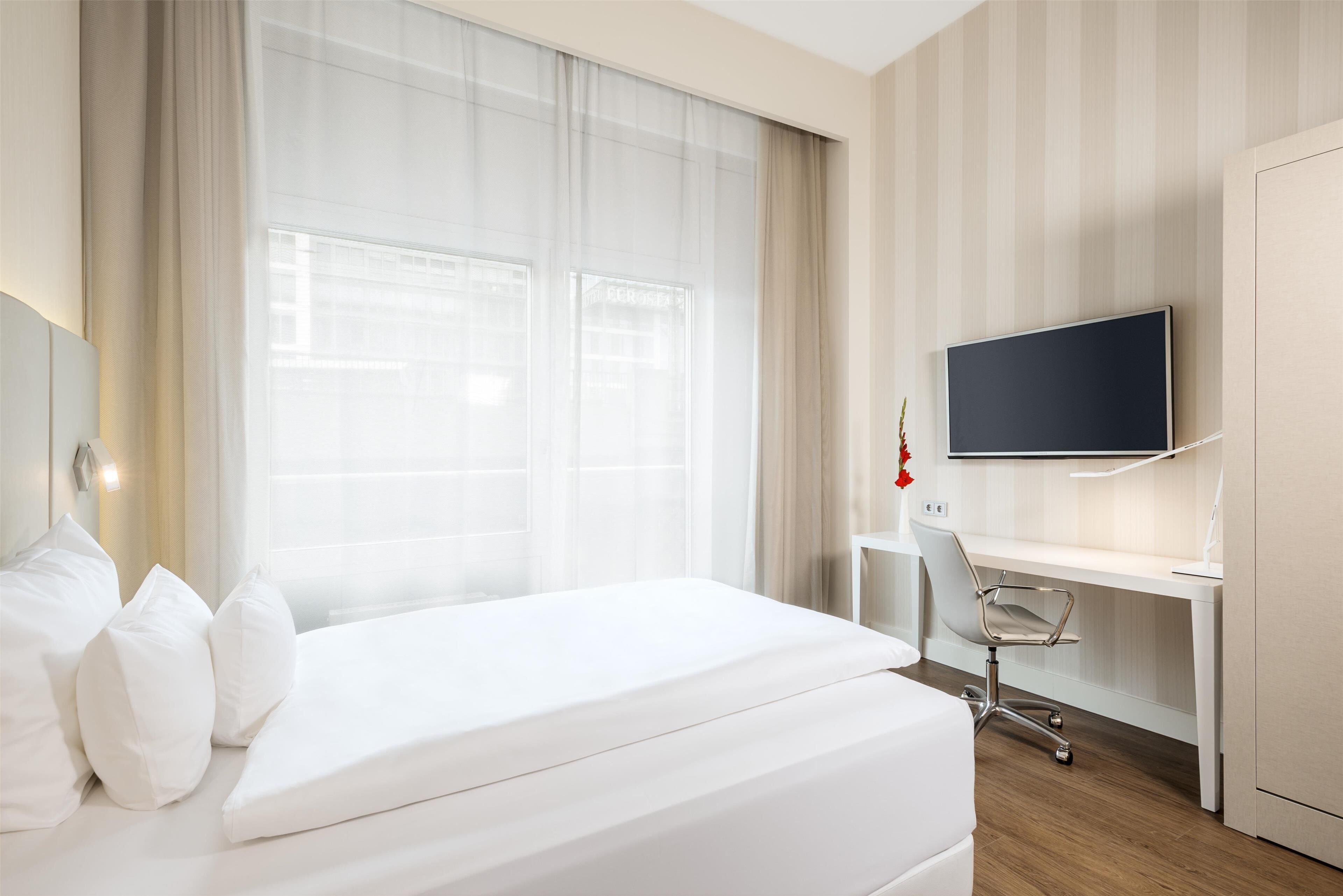 A hotel room with a bed, a desk, a chair, and a TV.