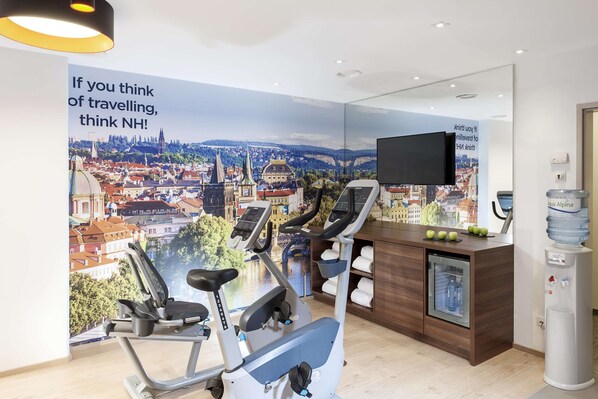 A gym with two stationary bikes, a water dispenser, and a large poster of a cityscape. - NH Collection Berlin Mitte Friedrichstrasse (Berlin)