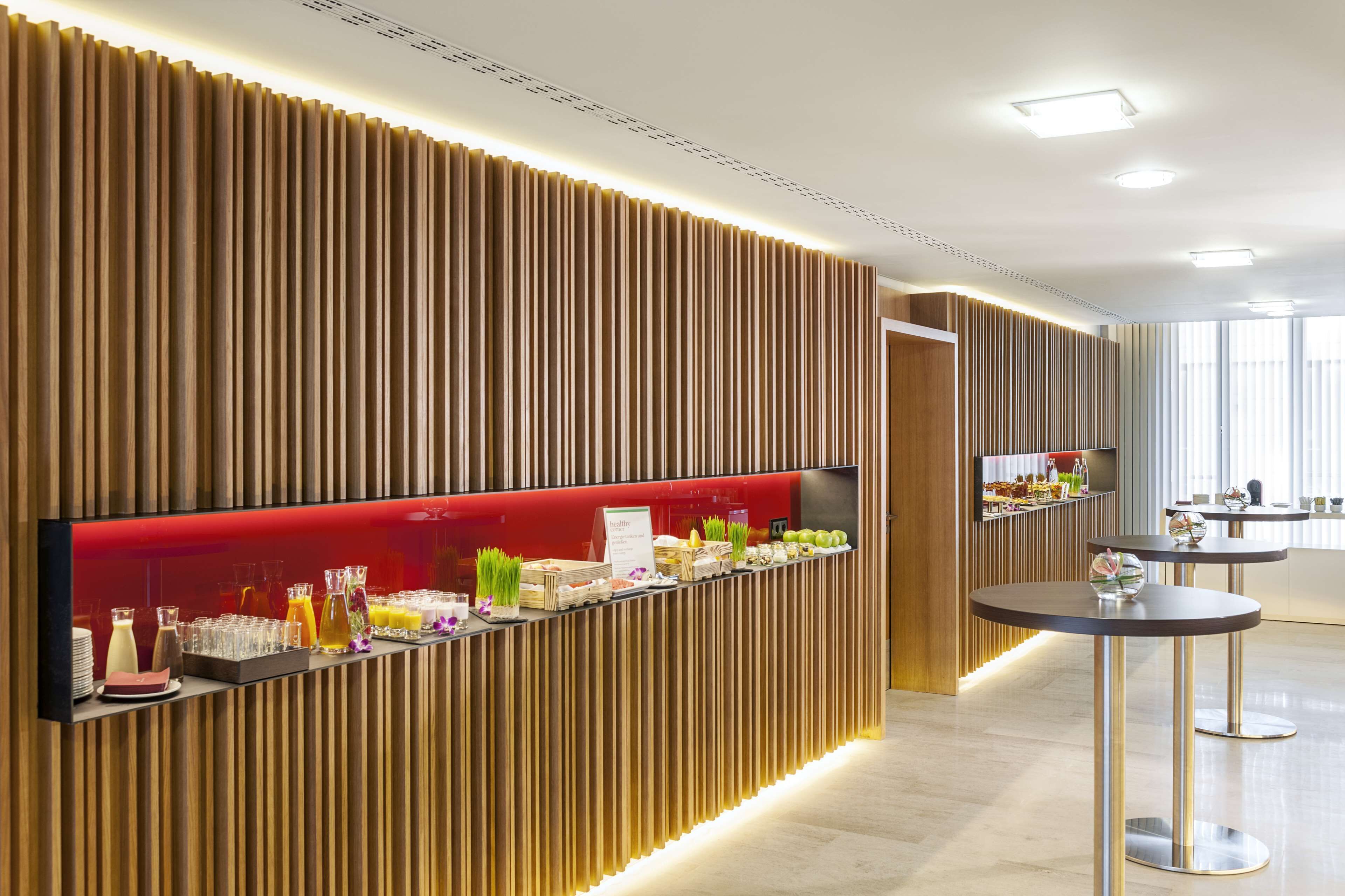 Una moderna zona de recepción con un panel de madera en la pared, una barra roja que ofrece bebidas y aperitivos, y un diseño limpio y minimalista.