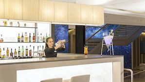Un bar moderno con una variedad de botellas de licor, un barman y un mural único con un cielo estrellado de fondo.