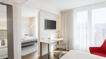 Una habitación de hotel con cama, escritorio, silla, televisión y ventana con cortinas.