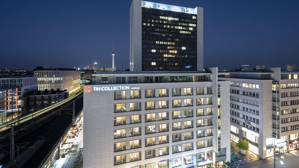 Un hotel moderno con varios pisos, un letrero destacado que dice "The Collection Hotels" y vistas de la ciudad, incluyendo una torre al fondo.
