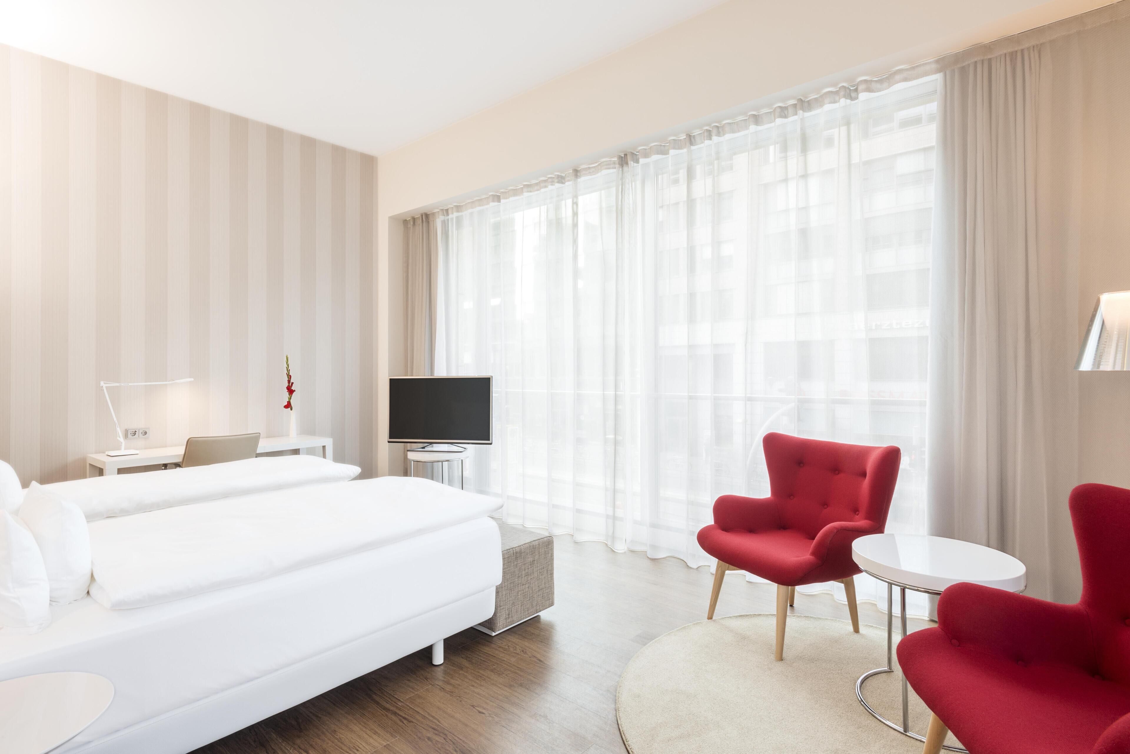 A hotel room with two beds, a TV, a desk, and a red chair.