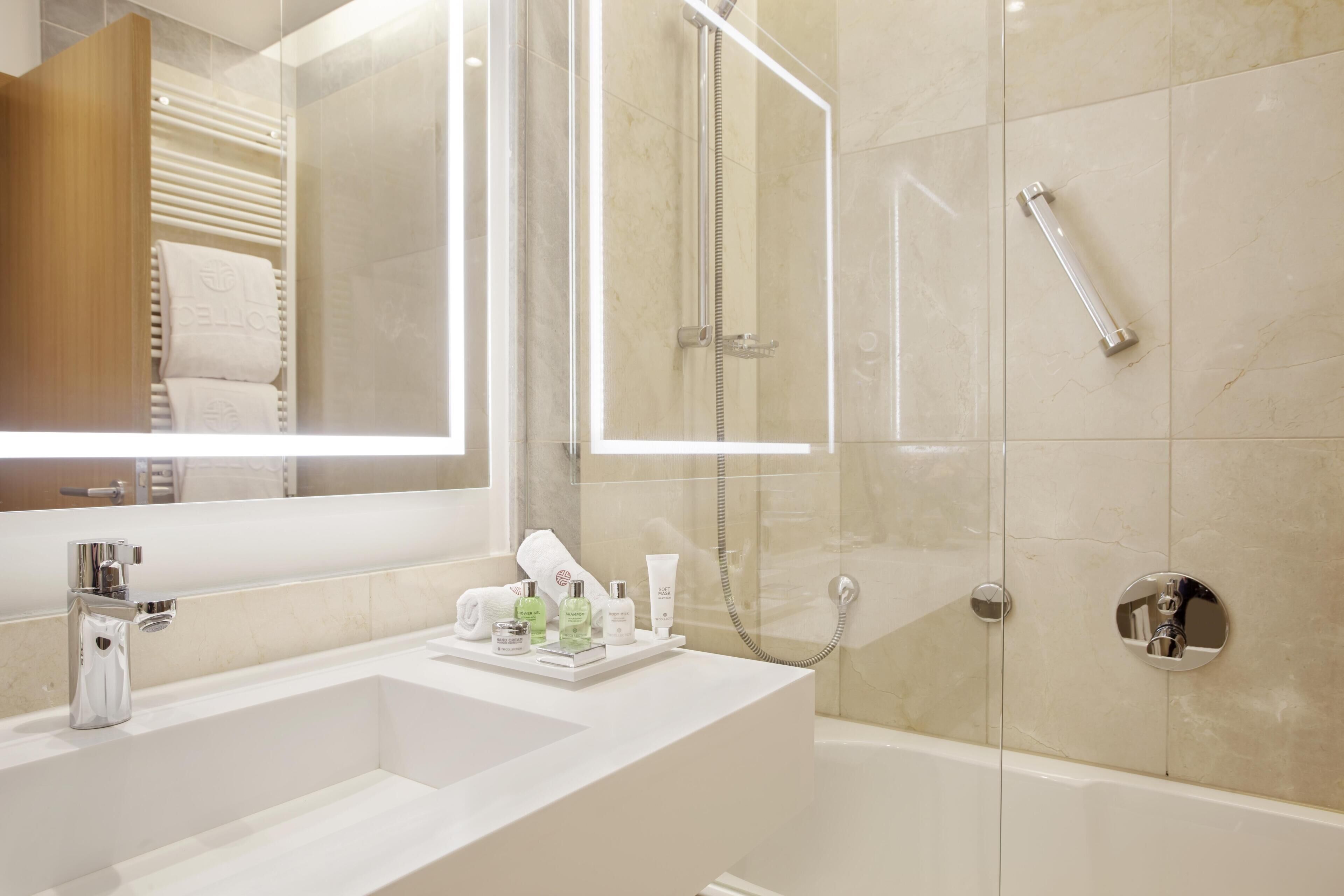 A modern bathroom with a large mirror, two sinks, a bathtub, and a glass-enclosed shower.