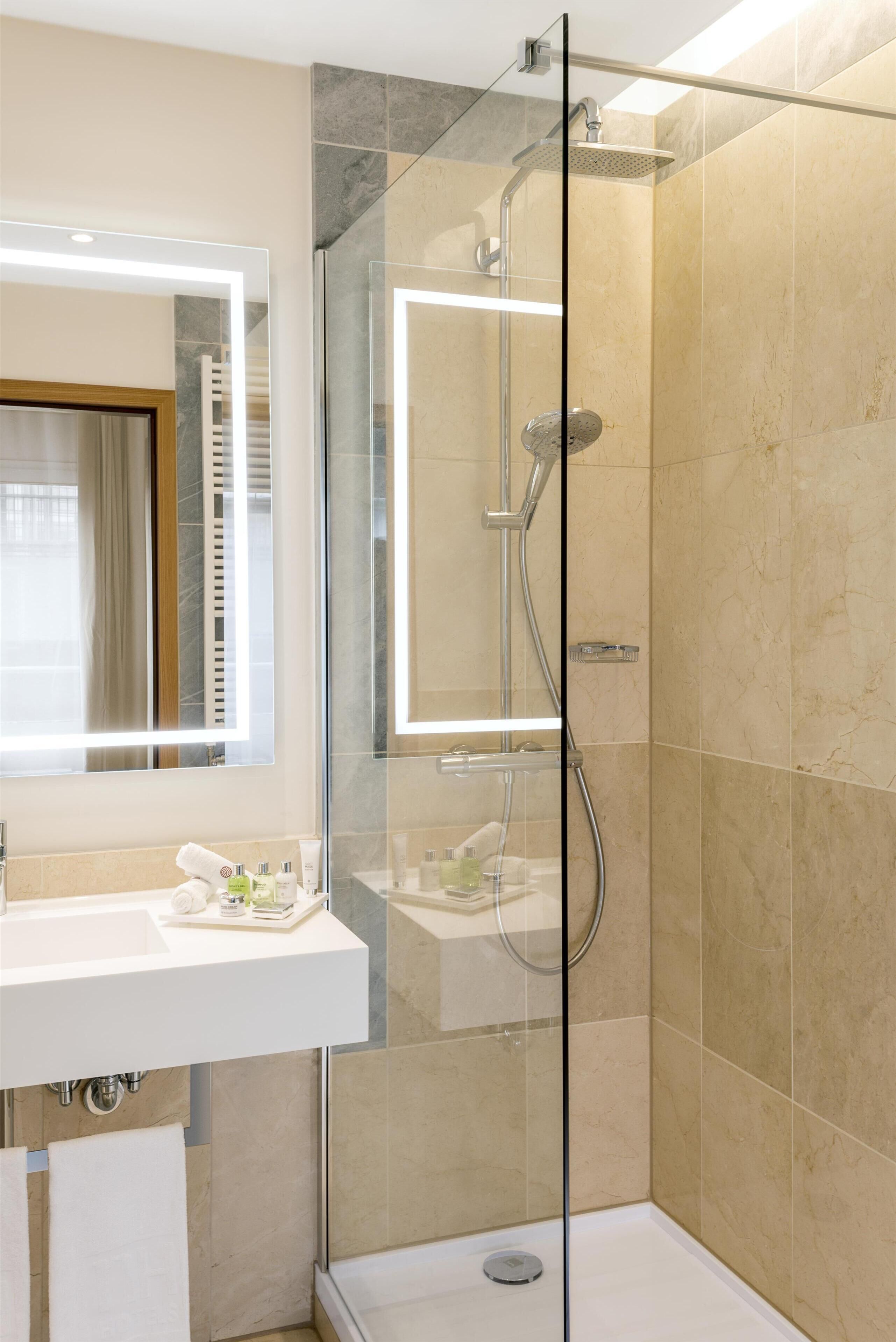 Une salle de bain moderne avec une douche à parois de verre, un lavabo blanc et un grand miroir.