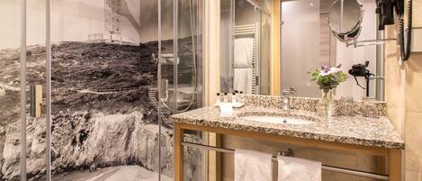 A bathroom with a granite countertop, a glass shower enclosure, and a large mirror.