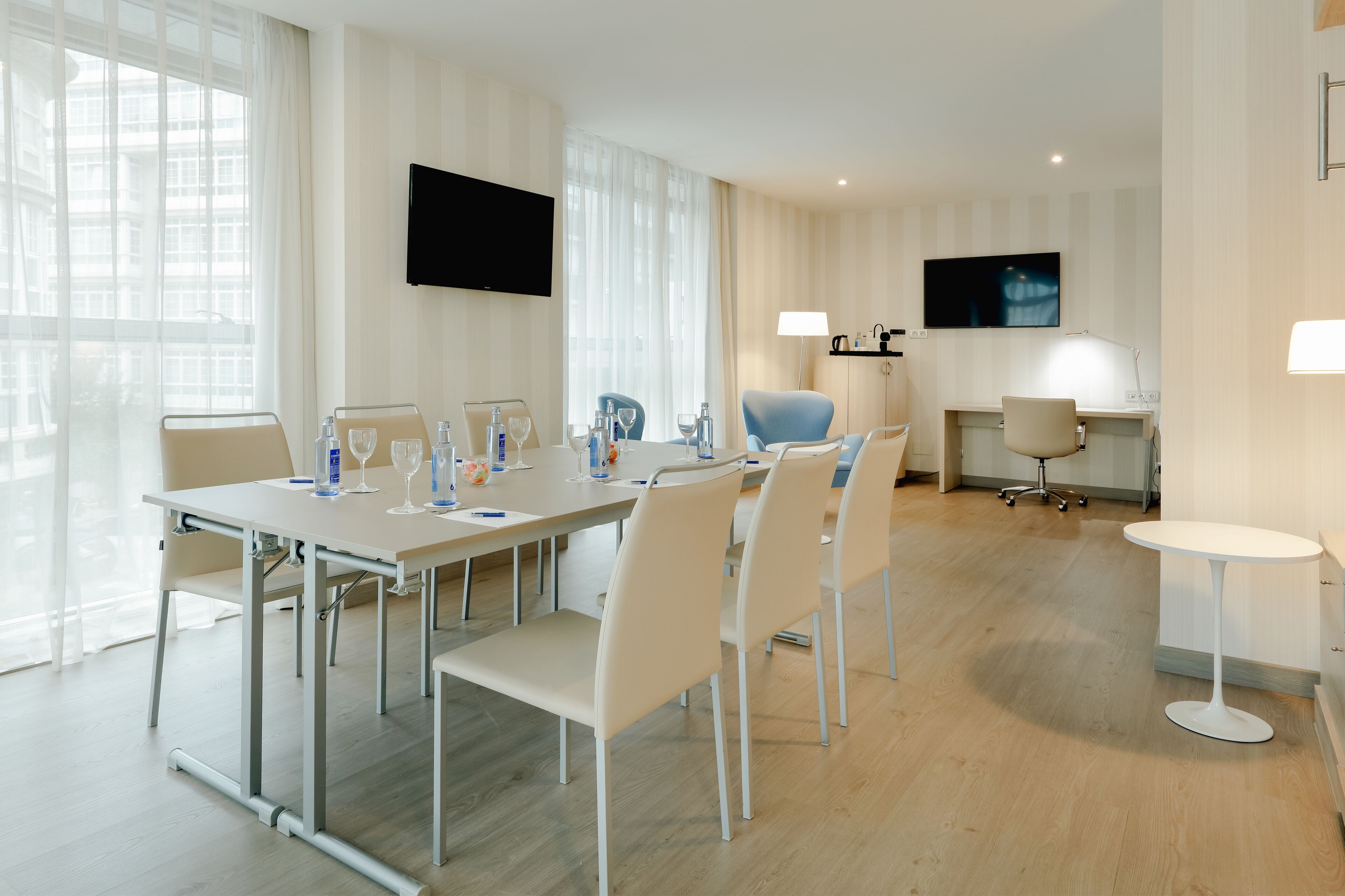 Een moderne hotelkamer met een grote eettafel, comfortabele stoelen, een aan de muur bevestigde televisie en een bureau met stoel.