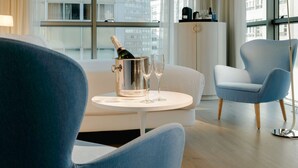A modern hotel room with a large window, a white sofa, a blue armchair, and a small round table with a champagne bottle and glasses. - Hesperia A Coruña Centro (A Coruña)