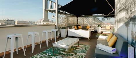 Una terraza en la azotea con sofá, taburetes de bar, una mesa y un tapete estampado.