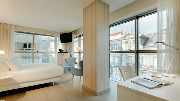 A modern hotel room with a bed, a desk with a cup and a book, a chair, and a TV. - Hesperia A Coruña Centro (A Coruña)