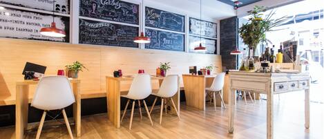 Un café moderno con mesas y sillas de madera, menús en una pizarra y lámparas colgantes.