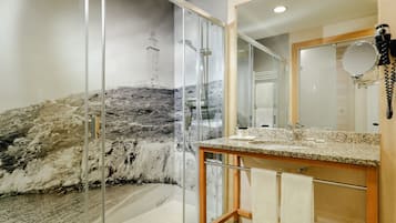 Baño con cabina de ducha de vidrio, encimera de granito y un espejo grande.