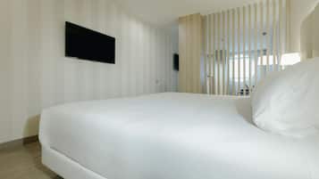 A hotel room with a large bed, a flat-screen TV mounted on the wall, and a window with vertical blinds.