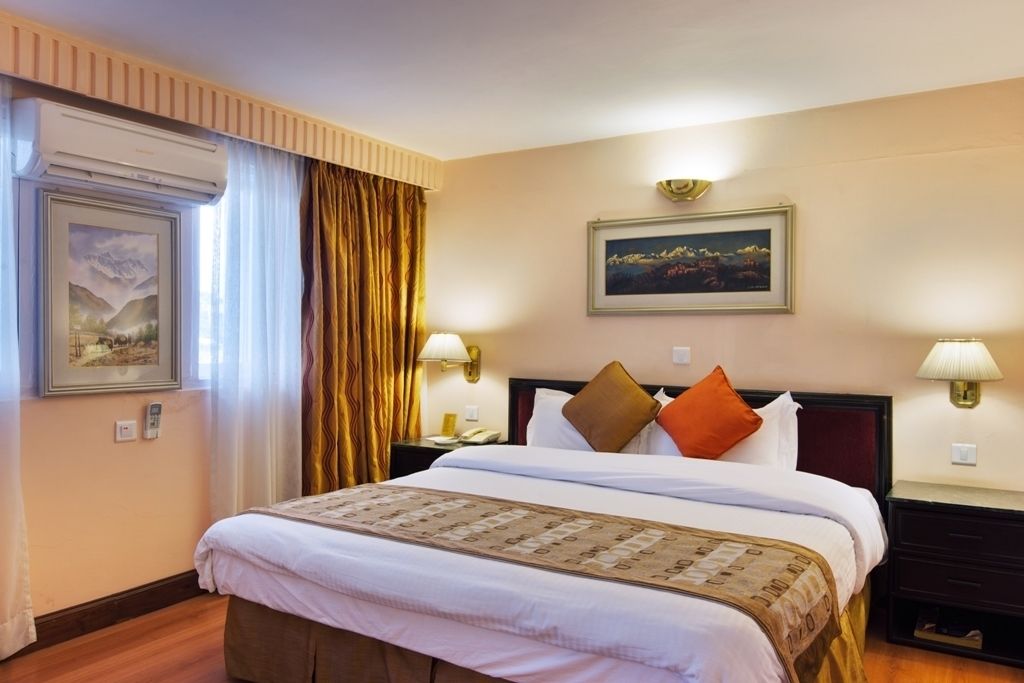 A hotel room with a bed, a nightstand, a lamp, a painting, and a window with curtains.