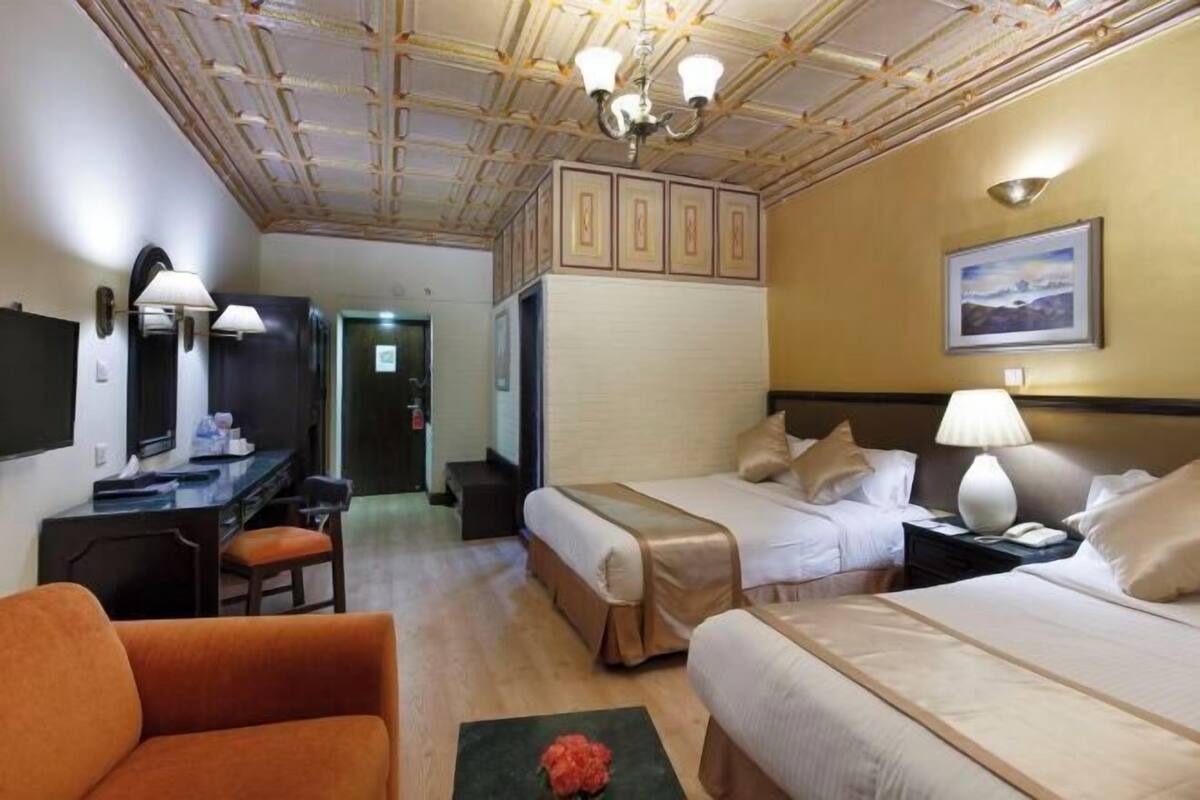 A hotel room with two beds, a desk, a chair, a television, and a framed picture on the wall.