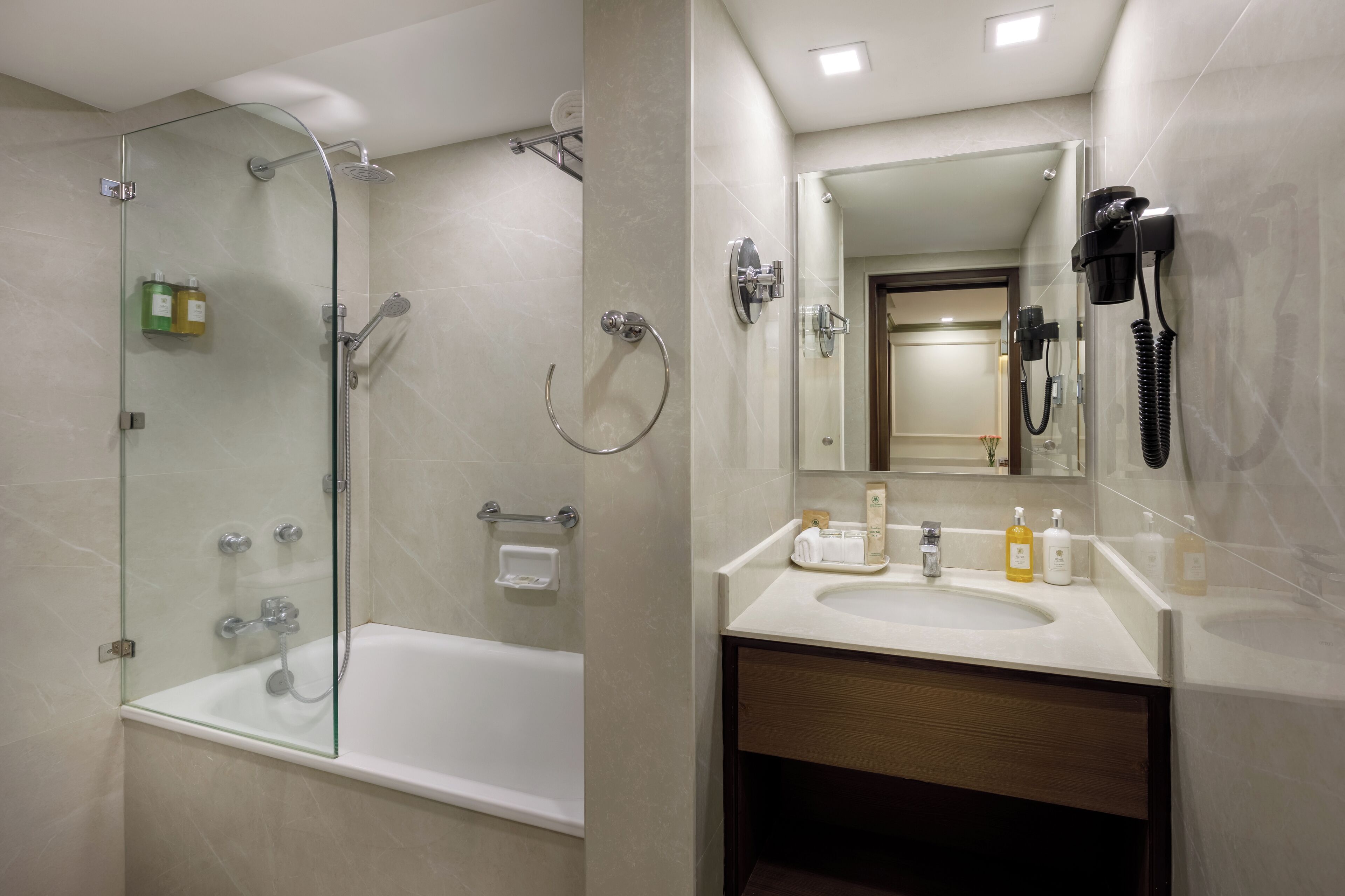 Un baño moderno con ducha envuelta en vidrio, una bañera independiente y un tocador con espejo, lavamanos y artículos de aseo.
