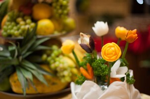 Una mesa con una composición de frutas y un florero con flores.