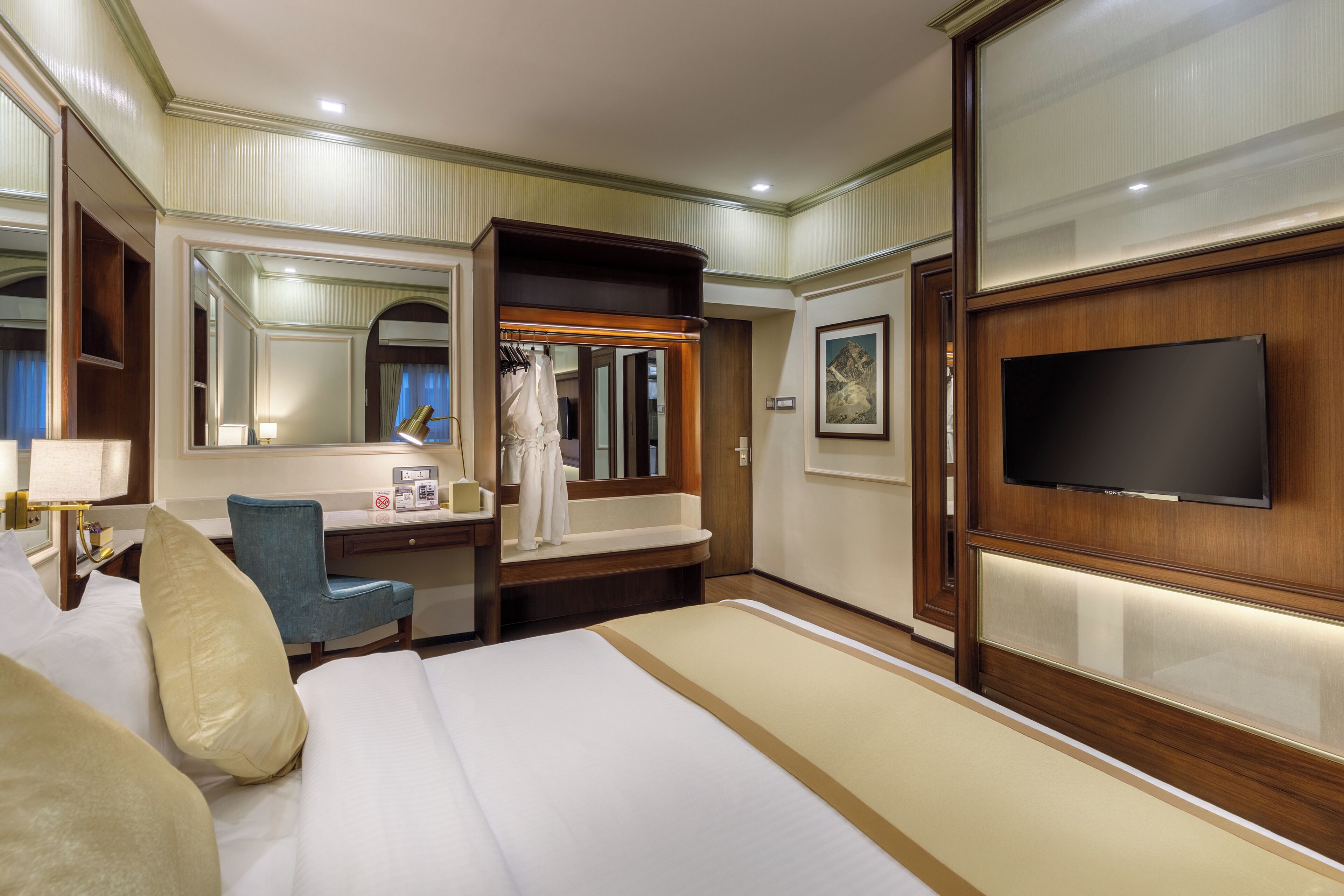 A hotel room with a large bed, a desk with a chair, a vanity with a mirror, and a television mounted on the wall.