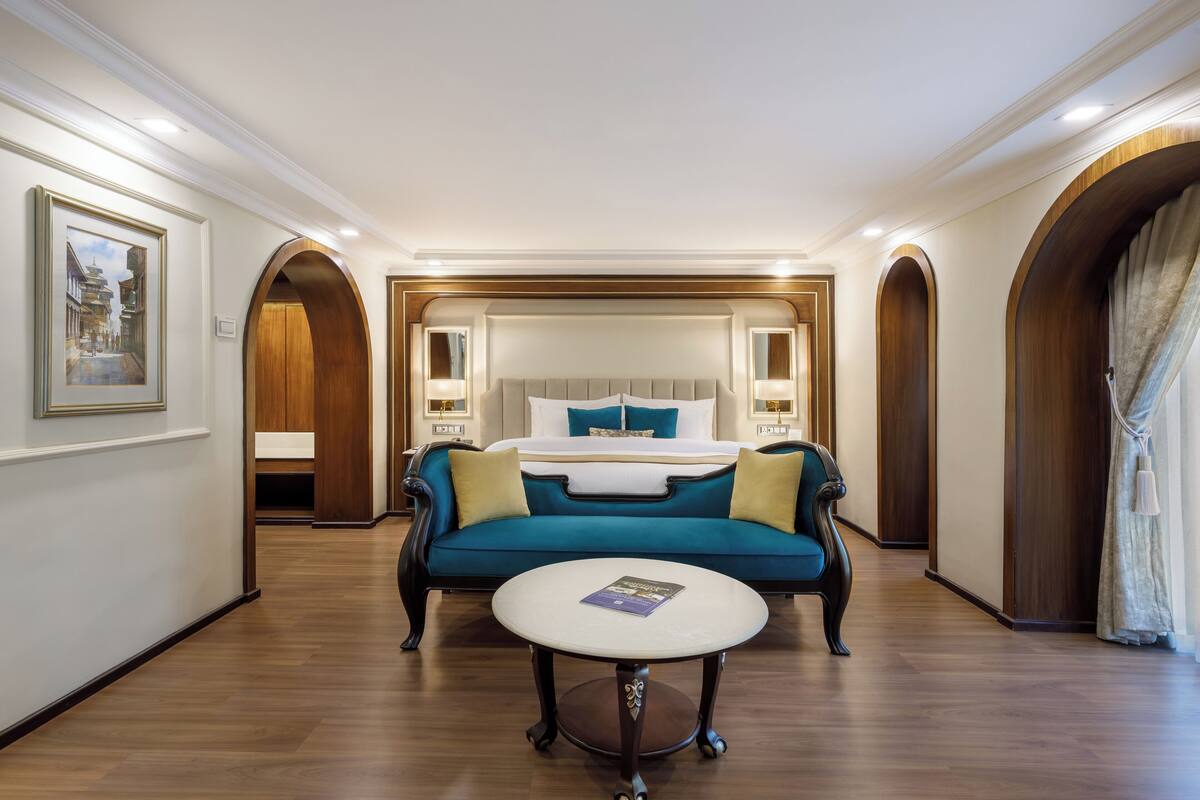 A hotel room with a large bed, a blue sofa, and a round table.