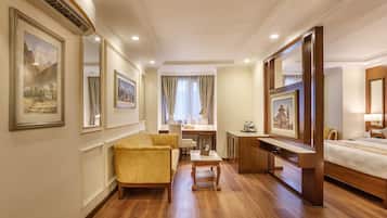 A hotel room with a wooden floor, a bed, a desk, a chair, a sofa, and framed artwork on the walls.