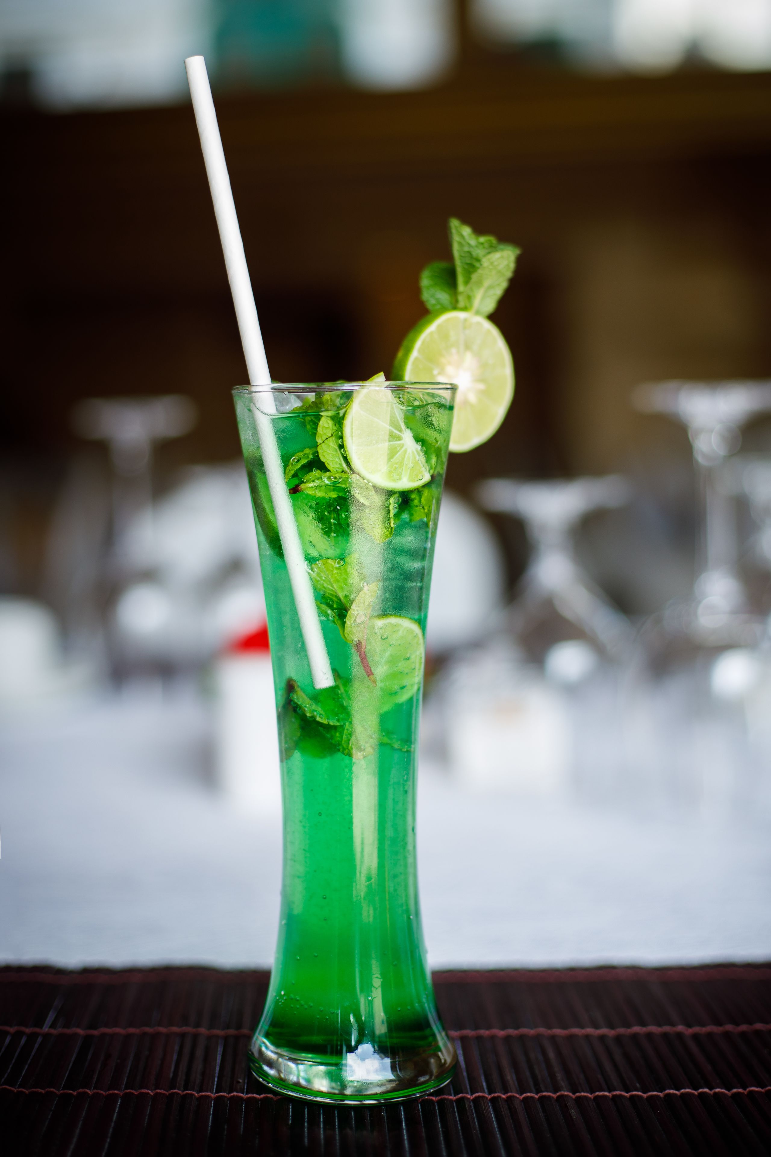 A tall glass with a lime slice and mint garnish, placed on a dark surface.