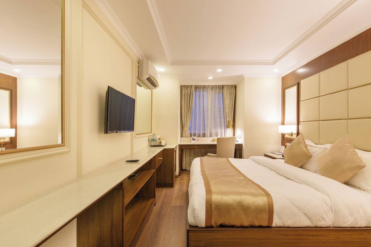 A hotel room with a bed, a desk, a chair, a television, and a large mirror.
