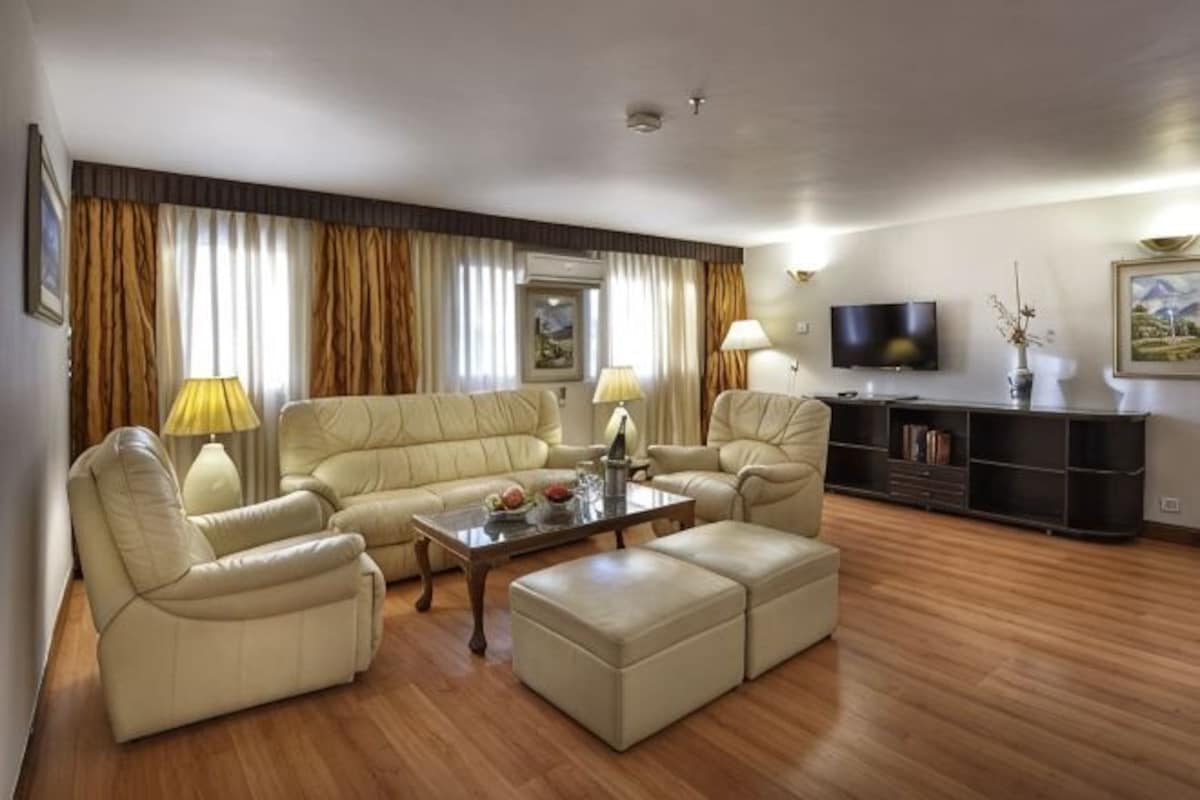 A living room with a sofa set, ottoman, coffee table, and a TV on a stand.