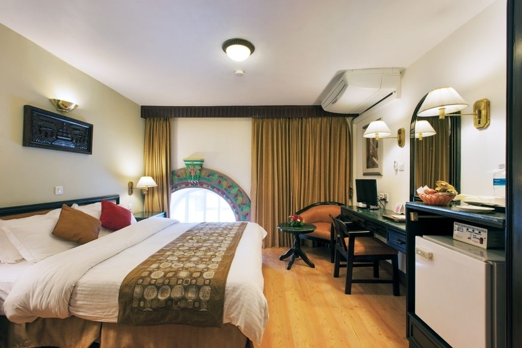 Una habitació d'hotel amb un llit, un escriptori, una cadira, una taula petita i un aparell d'aire condicionat.