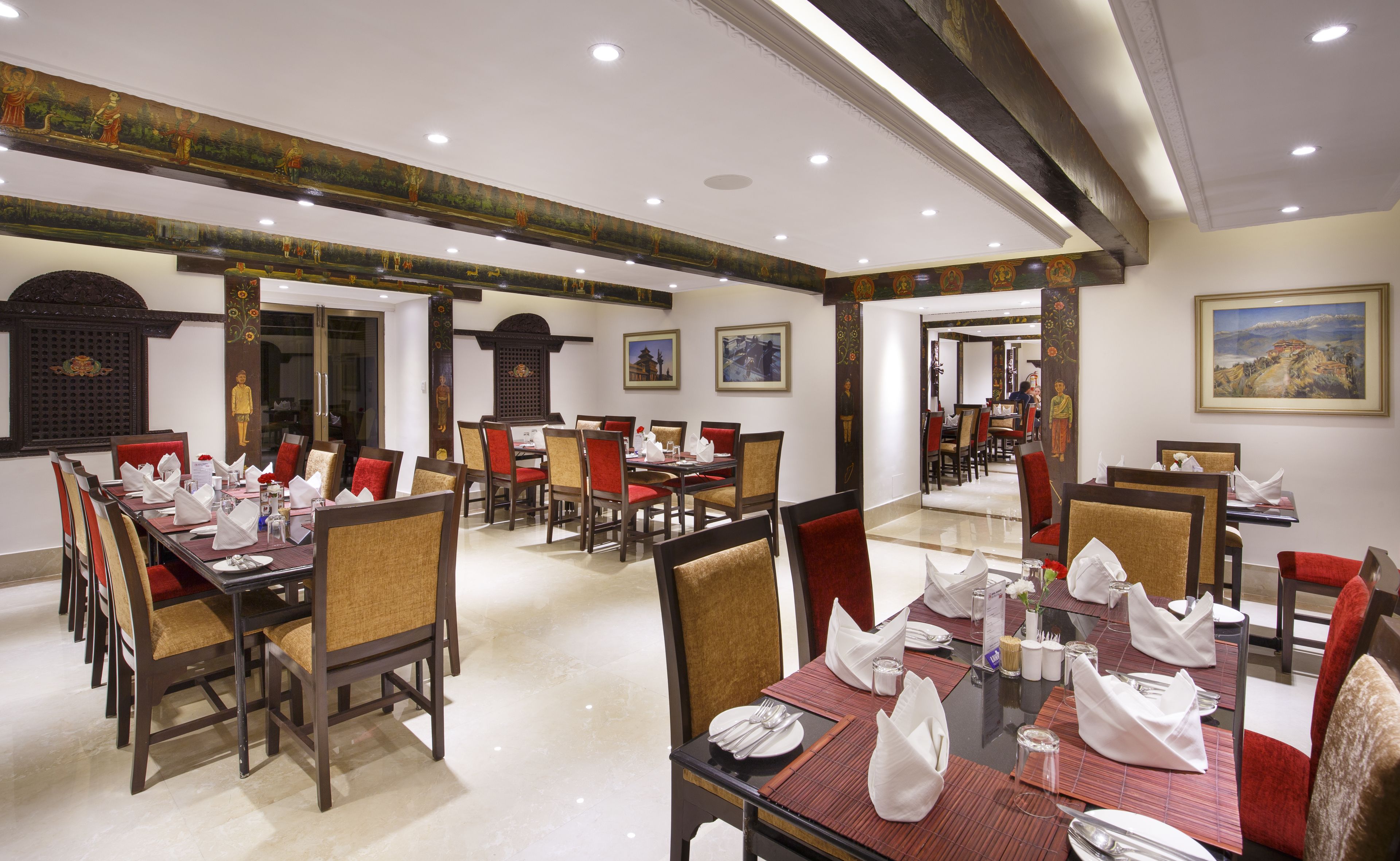 A spacious dining area with multiple tables and chairs, featuring traditional decor and artwork on the walls.