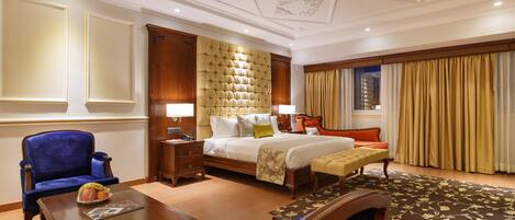 A hotel room with a large bed, a blue armchair, a wooden nightstand, and a small table with fruit.