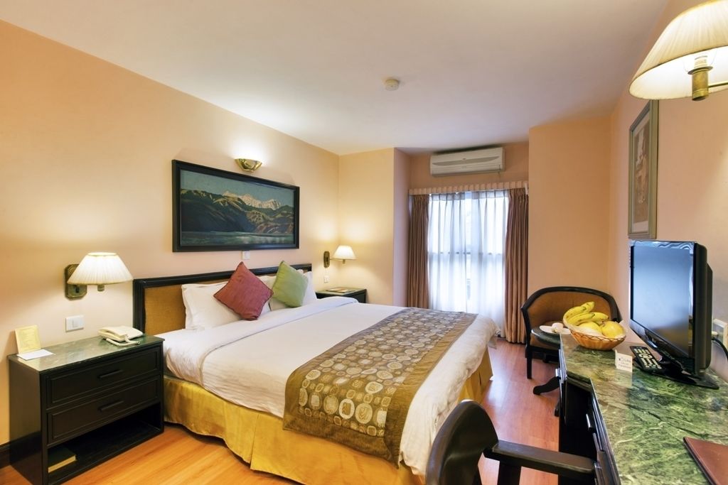 A hotel room with a bed, bedside tables, a desk with a chair, a television, and a window with curtains.