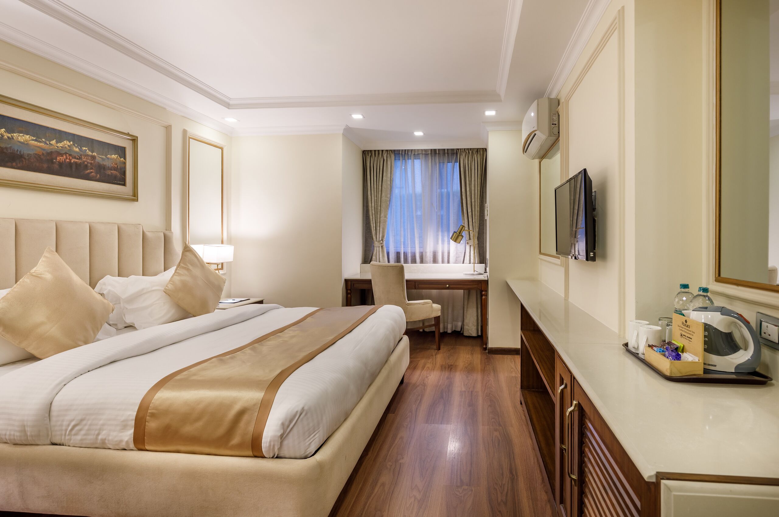 A hotel room with a large bed, a desk, a chair, a television, and a tray with toiletries.