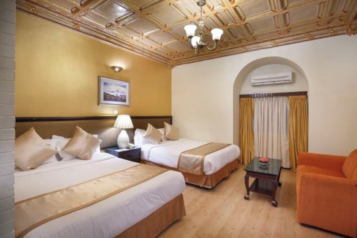 A hotel room with two beds, a sofa, a small table, an arched doorway, and a ceiling with a decorative pattern.