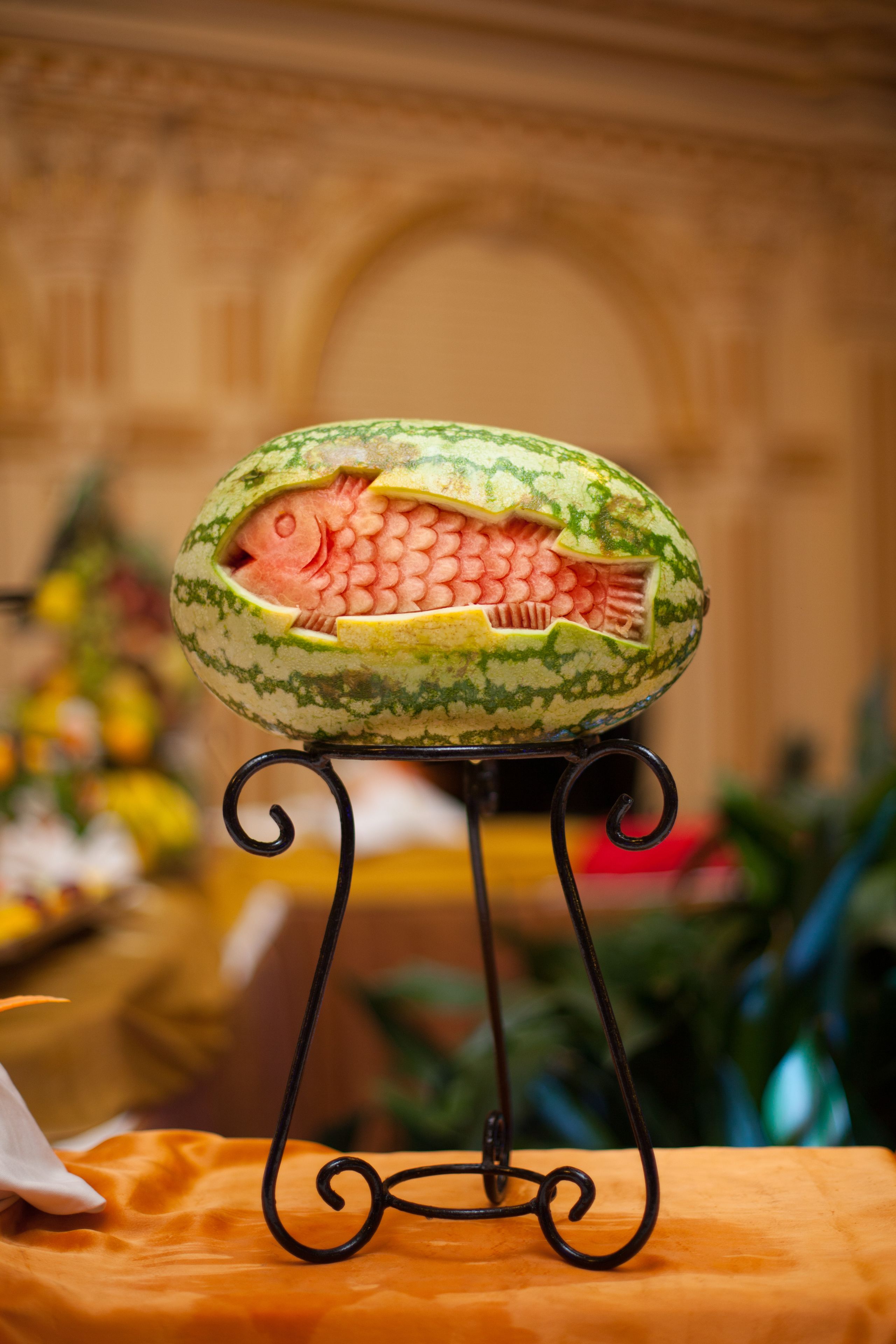 A watermelon carved to resemble a fish on a metal stand.
