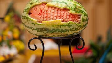 Wassermelone, kunstvoll geschnitzt als Fisch, auf einem Metallständer präsentiert.