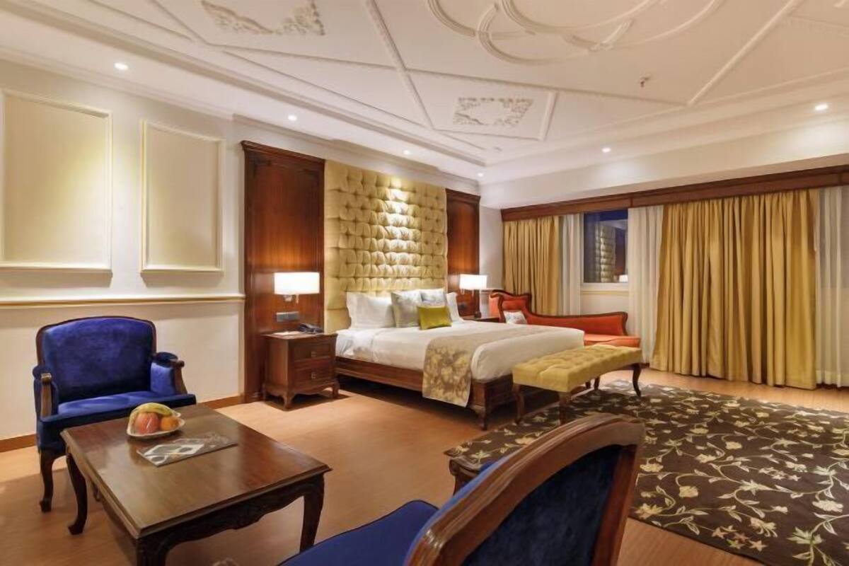 A hotel room with a large bed, a blue armchair, a wooden nightstand, a wooden table, and a patterned rug.