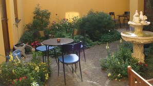 Une cour avec une table ronde et des chaises, entourée de plantes et de fleurs en pot.