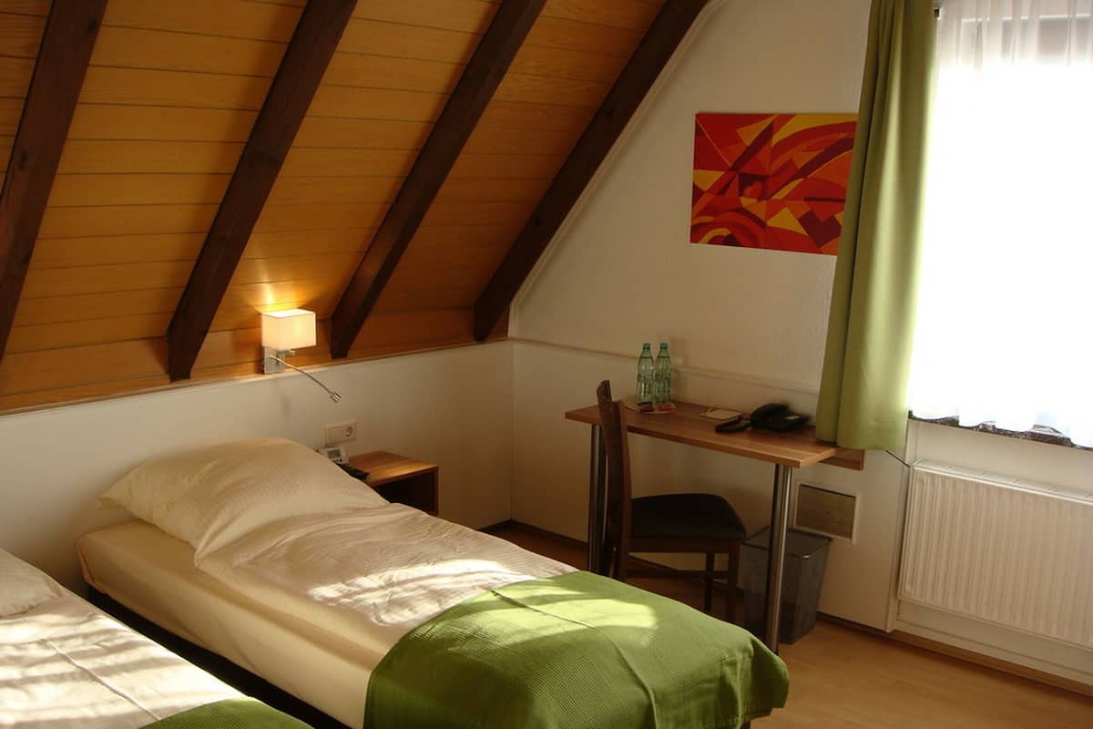 A room with two beds, a desk, a chair, a lamp, and a radiator.