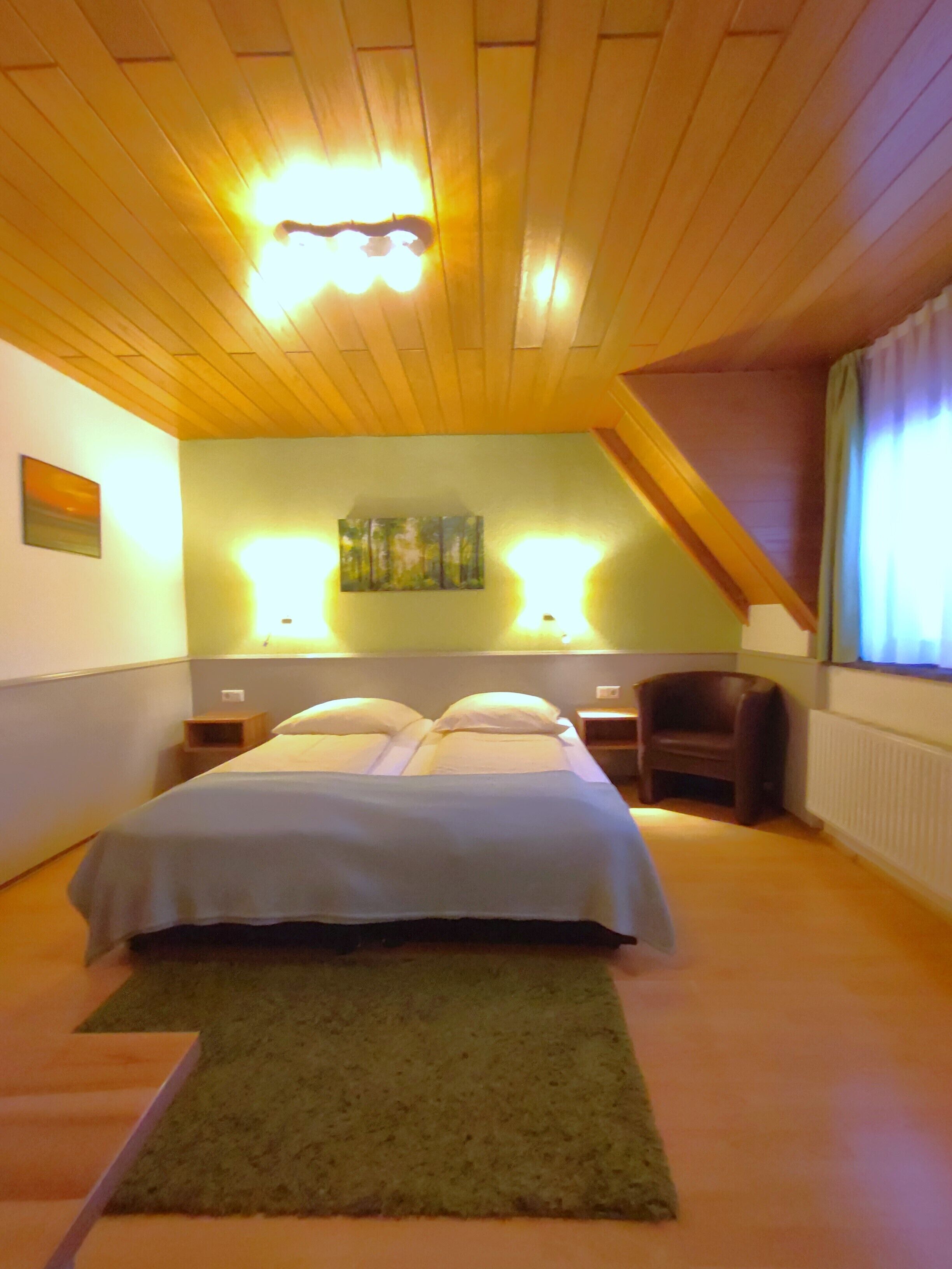 A bedroom with a bed, a chair, a painting, and a nightstand.