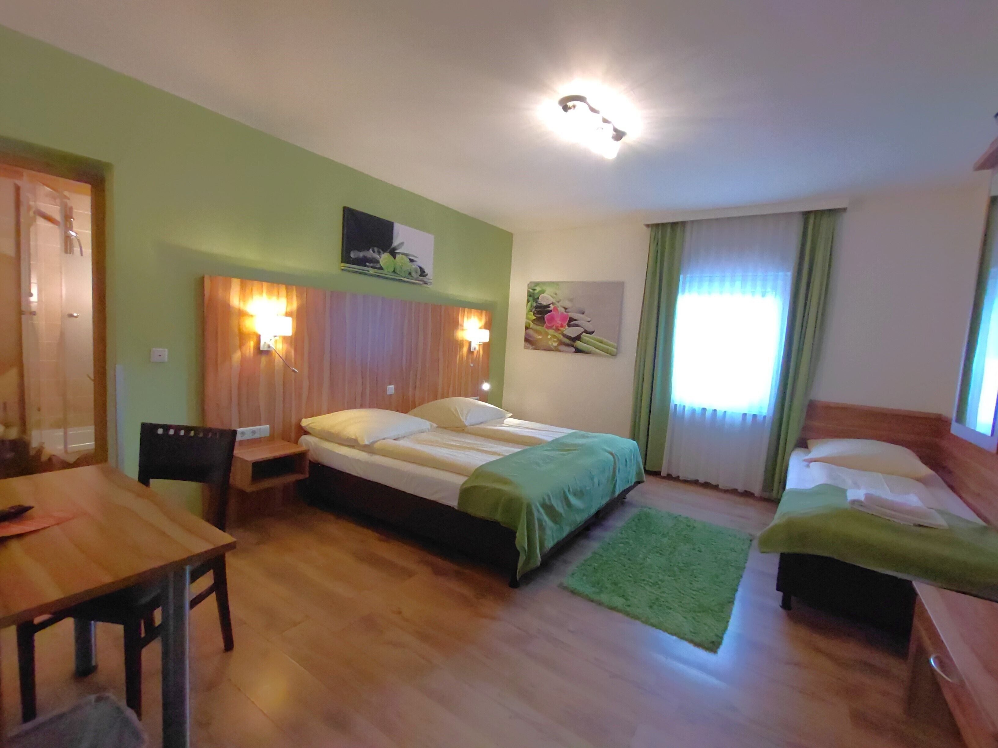 Une chambre d’hôtel avec un lit, un bureau et une chaise. Il y a une fenêtre avec des rideaux et un tableau au mur.
